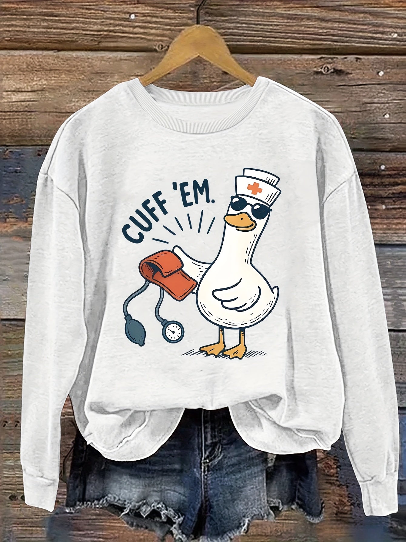 A cozy pink “Silly Goose” nurse sweatshirt featuring a cute duckling and bold CUFF ’EM slogan, perfect for winter shifts and everyday scrubs style.