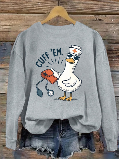 A cozy pink “Silly Goose” nurse sweatshirt featuring a cute duckling and bold CUFF ’EM slogan, perfect for winter shifts and everyday scrubs style.