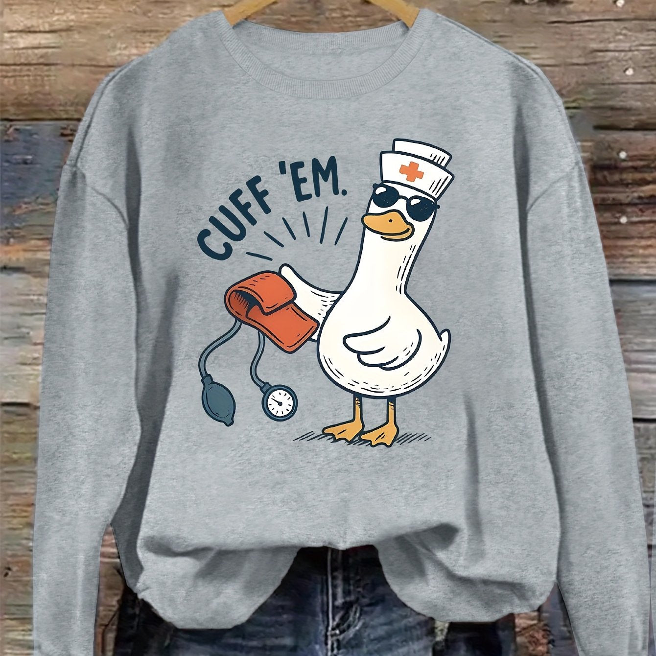 A cozy pink “Silly Goose” nurse sweatshirt featuring a cute duckling and bold CUFF ’EM slogan, perfect for winter shifts and everyday scrubs style.