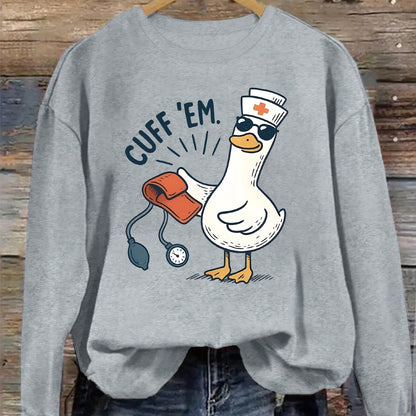 A cozy pink “Silly Goose” nurse sweatshirt featuring a cute duckling and bold CUFF ’EM slogan, perfect for winter shifts and everyday scrubs style.