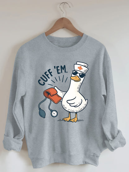 A cozy pink “Silly Goose” nurse sweatshirt featuring a cute duckling and bold CUFF ’EM slogan, perfect for winter shifts and everyday scrubs style.